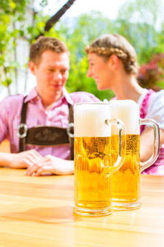 一对幸福的情侣坐在夏日的啤酒花园里，享受着一杯啤酒和阳光，在伏尔格伦站着两杯