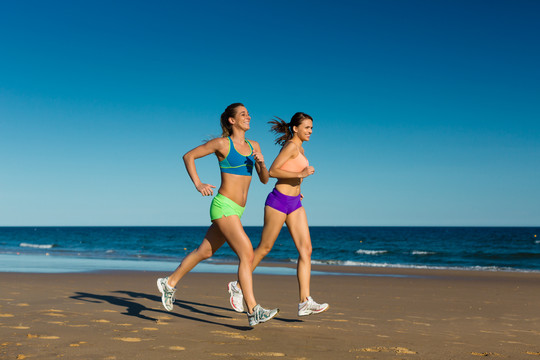 两个女人在海上度假时在沙滩上做运动，慢跑