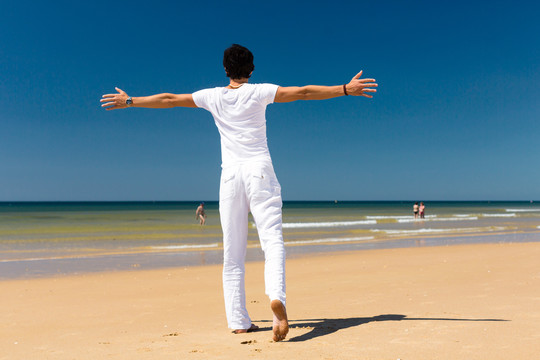 海边的帅哥在享受暑假，双臂伸向阳光象征着自由