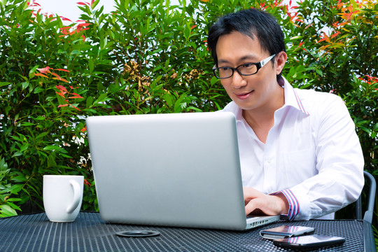 在户外工作的亚洲商人——他在用笔记本电脑工作，查看电子邮件