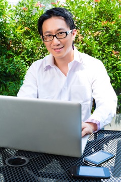 在户外工作的亚洲商人——他在用笔记本电脑工作，查看电子邮件