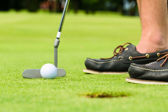 高尔夫球手把球放进洞里，只看到脚和铁