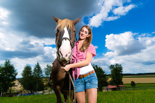 在多云的天空下，草地上牵着马的年轻女子