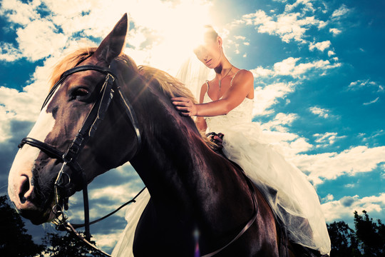 年轻的新娘穿着婚纱骑马，背光照照片，梦幻般的心情