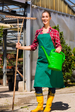 温室前的女商业园丁，带着水壶和耙子