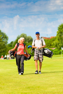 一对年轻的运动型夫妇在高尔夫球场上打高尔夫球，他们走向下一个洞