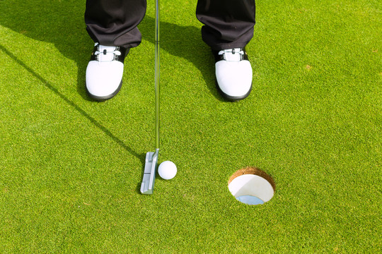 高尔夫球手把球放进洞里，只看到脚和铁