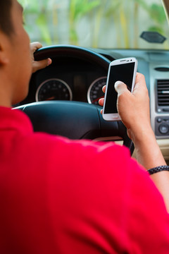 一名亚裔男子坐在车里，手里拿着手机边开车边发短信