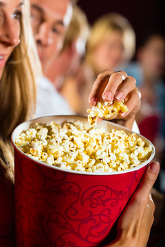 在电影院或电影院里吃大容器爆米花的女人