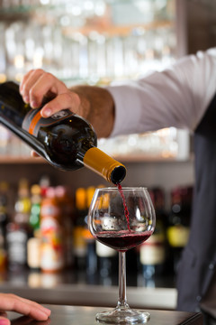 酒保在餐厅或酒店的吧台上用玻璃杯倒红酒