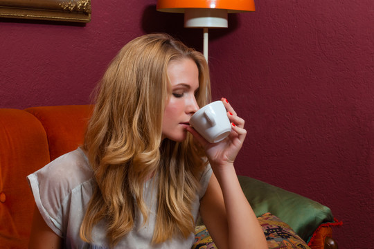 年轻女子坐在老式咖啡馆的沙发上，喝着一杯咖啡