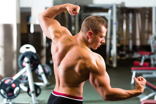 强壮的男人，在健身房摆姿势的健美运动员，背景是健身器材