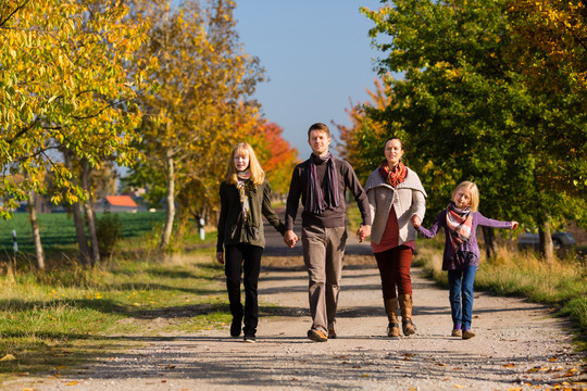 一个年轻的家庭，带着母亲、父亲和女儿在秋天或秋天穿过五颜六色的树