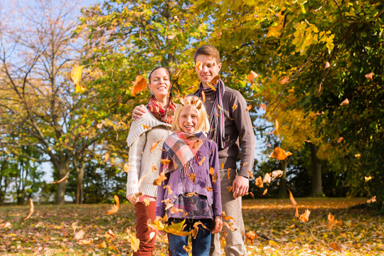 幸福的家庭，母亲，父亲和女儿或孩子站在户外与五颜六色的树叶和树下在秋天或秋天
