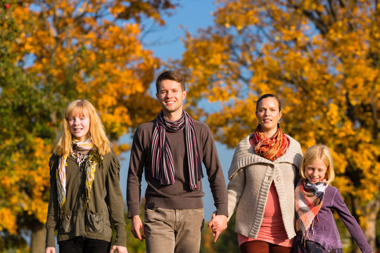 一个年轻的家庭，带着母亲、父亲和女儿在秋天或秋天穿过五颜六色的树
