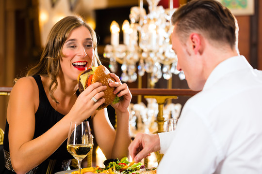 一对男女在一家高级餐厅吃快餐、汉堡和薯条，背景是一盏大吊灯
