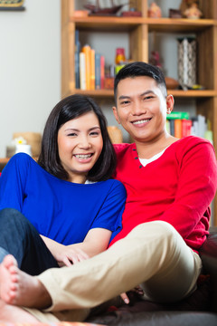 印度尼西亚的一对年轻夫妇——男人和女人——坐在家里的沙发上，这是周末，他们享受着闲暇时光