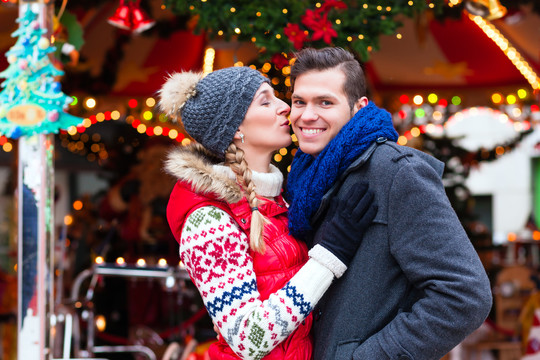 男人和女人或一对夫妇或朋友在降临节或假日在旋转木马前或结婚在圣诞节或圣诞节市场上转