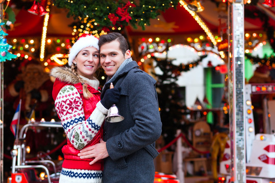 男人和女人或一对夫妇或朋友在降临节或假日在旋转木马前或结婚在圣诞节或圣诞节市场上转