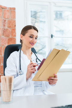 年轻的女医生坐在诊所窗户前的书桌旁看文件或档案
