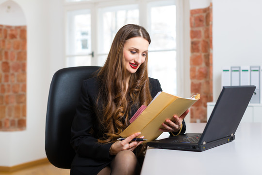 年轻的女商人或秘书在办公室工作，在笔记本电脑上写字