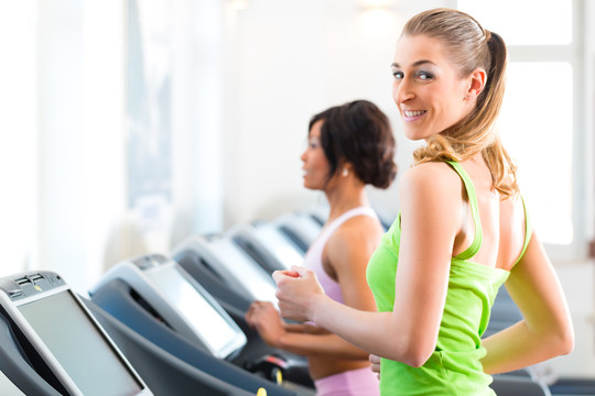 在健身房或健身俱乐部的跑步机上跑步-两个女人锻炼以获得更多的健身