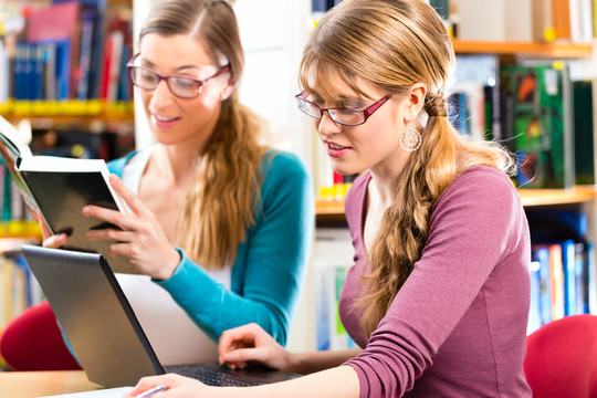 学生-在图书馆的年轻女性与笔记本电脑和书籍学习小组