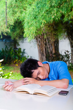 年轻的中国亚裔学生在家里厌倦了第二天的家庭作业，他已经睡着了