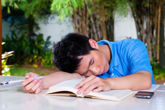 年轻的中国亚裔学生在家里厌倦了第二天的家庭作业，他已经睡着了