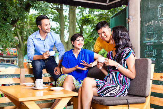 亚洲朋友或同事在咖啡馆享受休闲时光，喝咖啡或卡布奇诺，在平板电脑上看照片或电子邮件