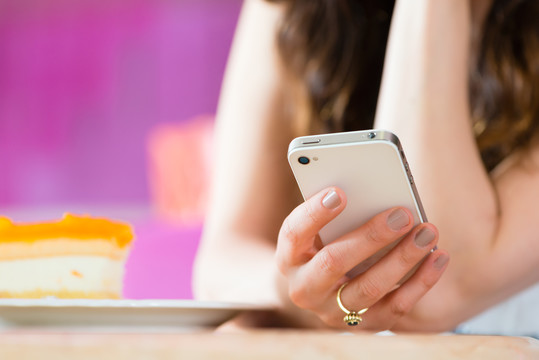 年轻女子在咖啡馆或冰淇淋店使用她的手机，也许她是单身或等待某人