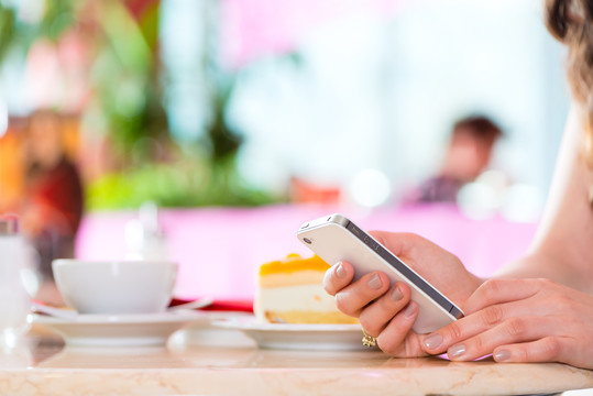 年轻女子在咖啡馆或冰淇淋店使用她的手机，也许她是单身或等待某人