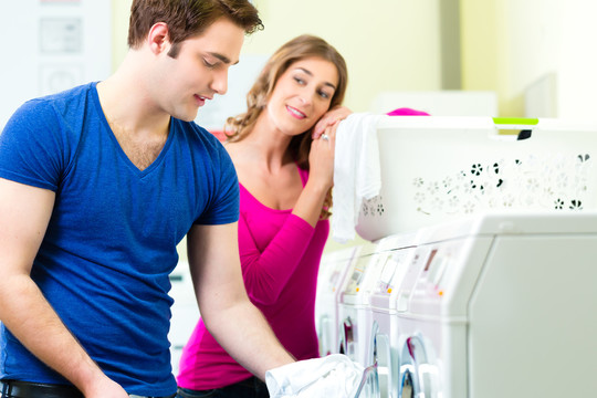 人们在洗衣房里洗他们的脏衣服，背景是洗衣机