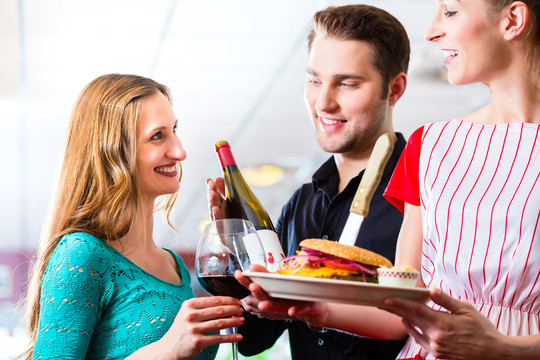 在美式快餐店吃快餐的朋友或夫妇，服务员提供食物、汉堡、薯条和红酒