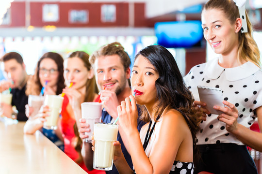 朋友或情侣在美式快餐店的吧台上吃快餐、喝奶昔，服务员正在点菜