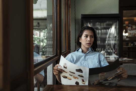 一位泰国亚裔女子坐在咖啡馆里看甜点菜单。