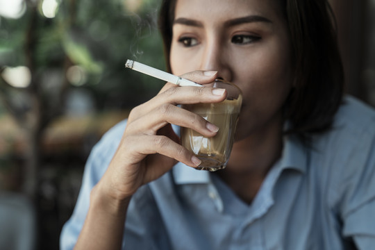 特写亚泰妇女吸烟和喝咖啡拿铁从玻璃杯。