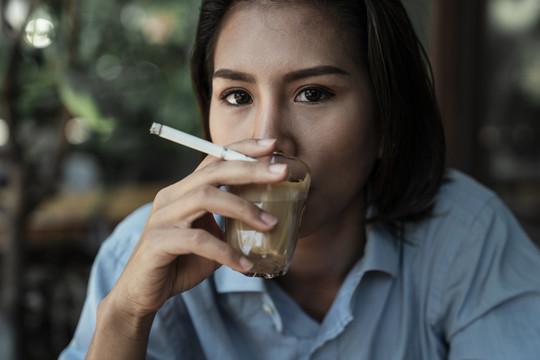 特写亚泰妇女吸烟和喝咖啡拿铁从玻璃杯。