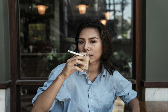 穿蓝衬衫的亚泰女人一边抽烟一边喝热咖啡。