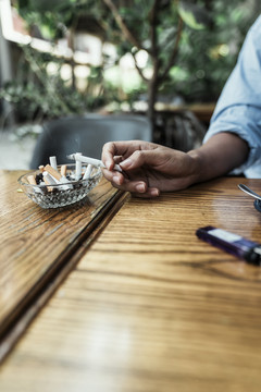 一个不健康的女人用手把香烟上的烟灰抖到木桌上的烟灰缸里。