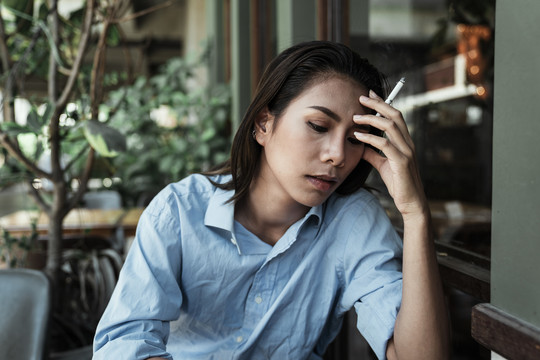 一名身穿蓝色连衣裙、手持香烟的泰国亚裔女子情绪低落。