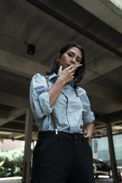 穿蓝衬衫的泰国亚裔女商人在大楼地下室抽烟。