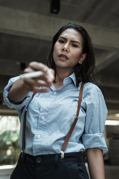 穿着蓝色衬衫、满脸愁容的亚洲女人拿着香烟指着镜头。