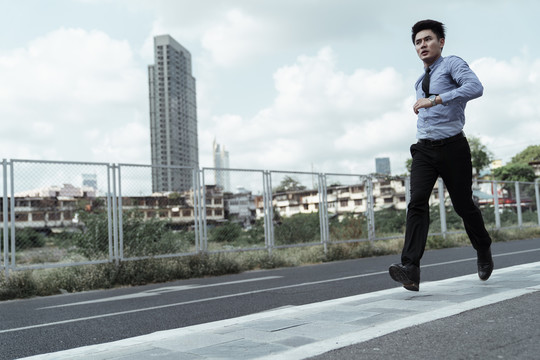 年轻的亚洲商人穿着正装在城市跑道上跑步。在城里锻炼的亚洲商人。