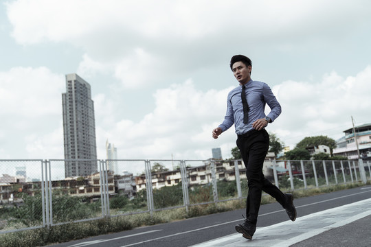 年轻的亚洲商人穿着正装在城市跑道上跑步。在城里锻炼的亚洲商人。