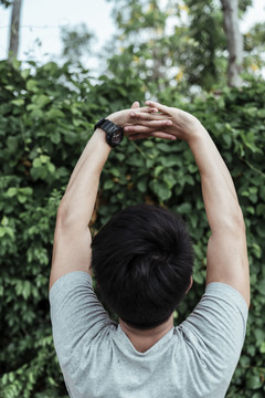 亚洲年轻人在公园里伸展双臂的后视图。