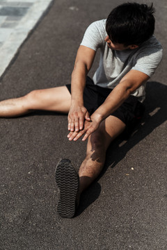 一个年轻的亚洲运动员坐在地上伸着手想摸他的脚。坐着伸展。