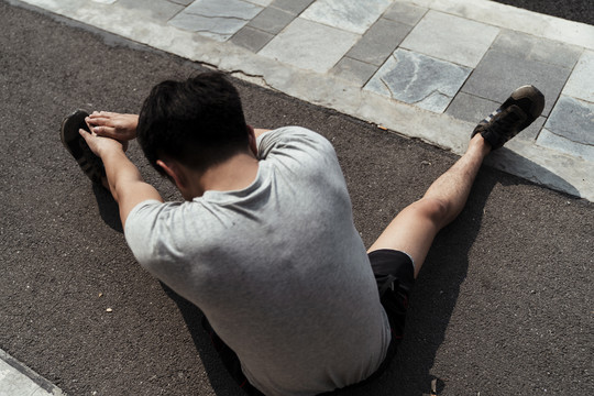 一个年轻的亚洲运动员坐在地上伸着手想摸他的脚。坐着伸展。
