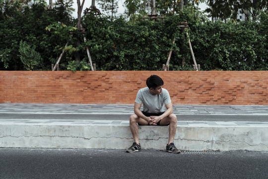 沮丧的男人独自坐在靠近城市街道的人行道上。孤独的人在路上。