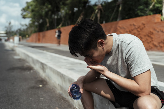 运动男用瓶子里的水洗脸。亚洲年轻人用瓶子里的水洗脸。